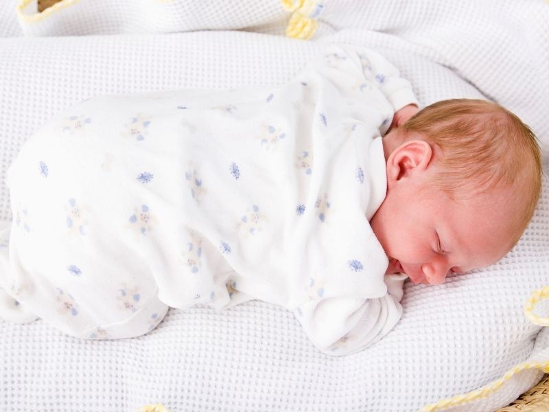 A newborn boy is sleeping on his tummy, in his crib, with nothing else around him (to prevent SIDS)