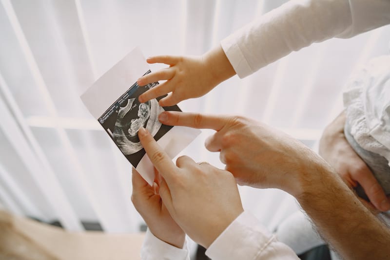 Parents and their toddler child are looking at a recent ultrasound of the new baby to be.