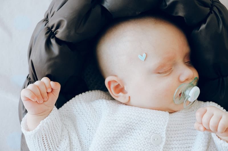 An infant girl is sleeping on her back with a pacifier in her mouth