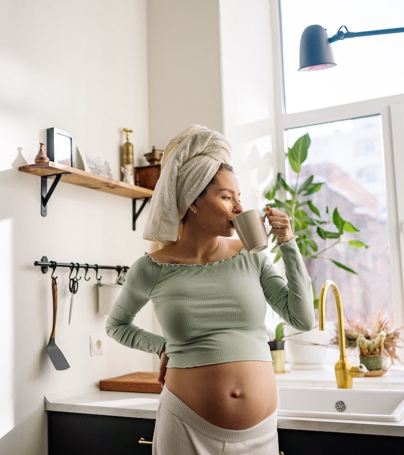 A pregnant woman is drinking water from a mug to stay hydrated