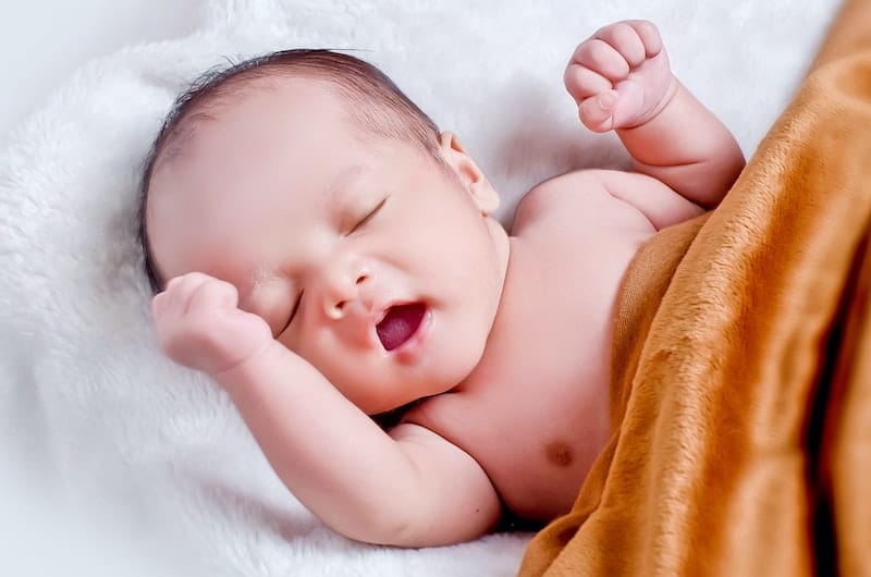 A newborn baby is laying on his back with his eyes closed