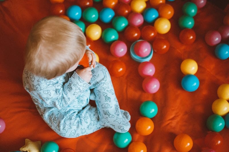 An infant boy is sitting up playing with his toy balls