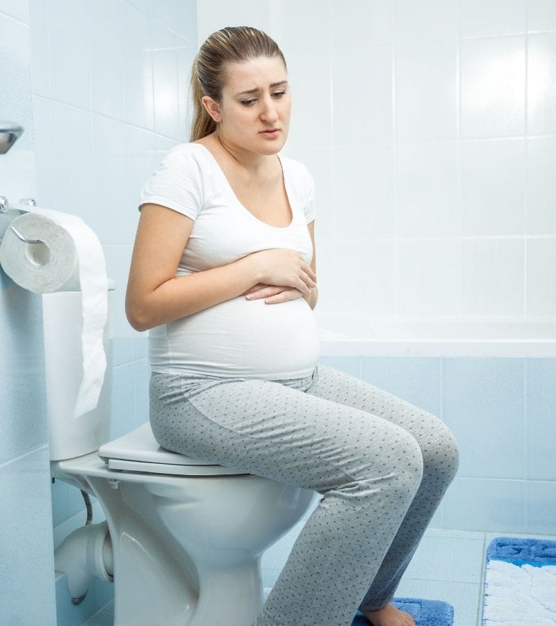 A pregnant woman is sitting on the toilet frustrated because she's constipated