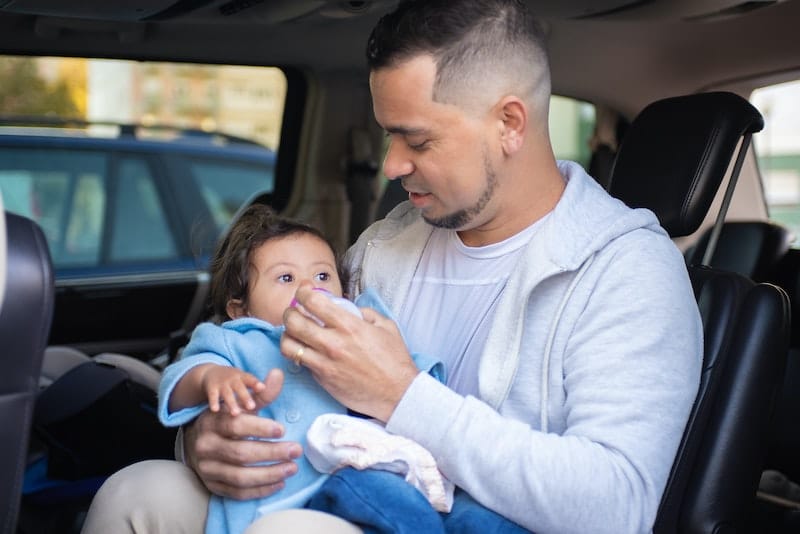 Dad is bottle feeding his infant daughter formula milk in their parked car