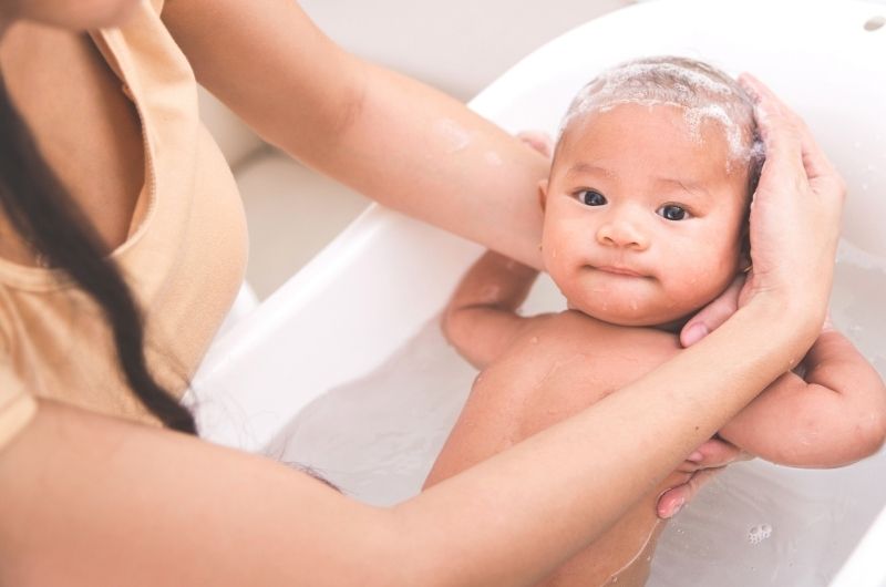 Mom is applying shampoo that has tea tree oil on her infant son's scalp to help with cradle cap