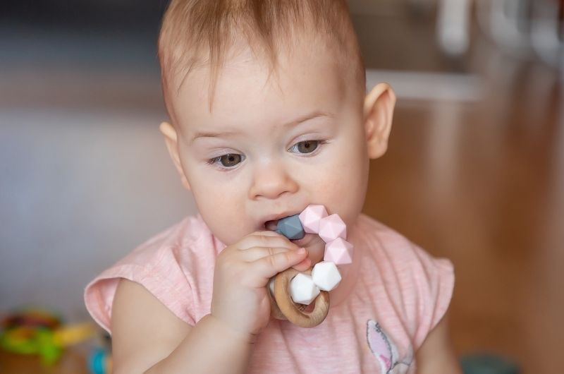 A one-year-old girl is using a teething toy to help with her tooth eruption discomfort