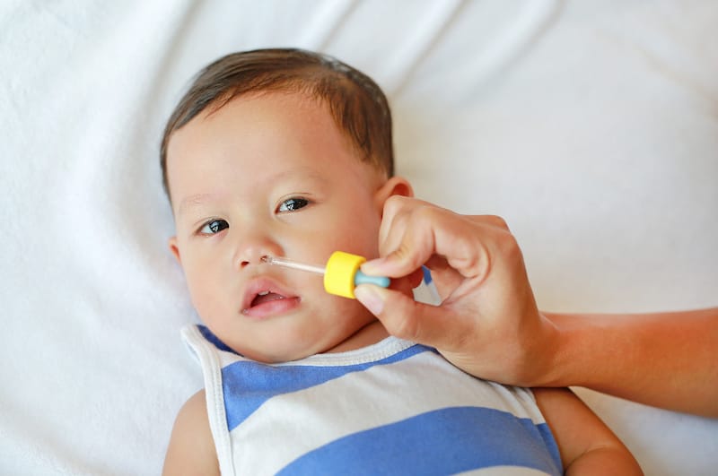Mom is putting saline drops in her infant son's nose to help loosen up the mucus so her baby can breathe better