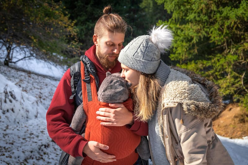 A young German couple is taking a walk in the cold winter while dad holds their infant baby in a baby body carrier