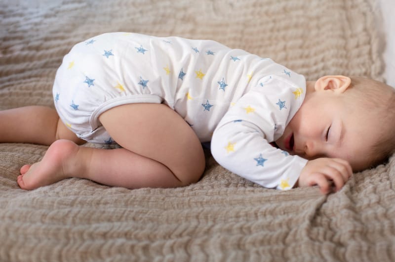 An infant baby is sleeping on his knees, also known as the frog sleep position for babies.