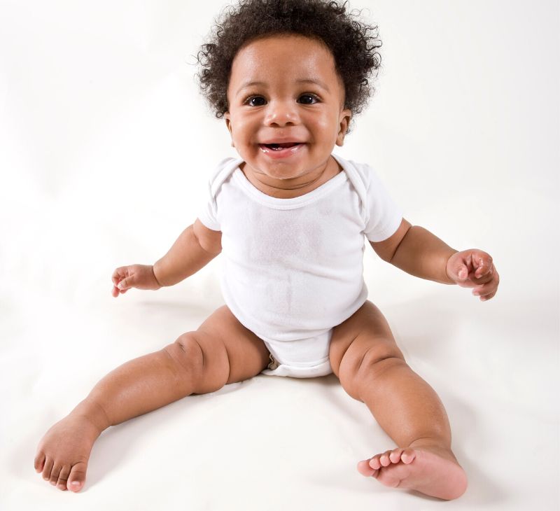 An infant boy is sitting up and is practicing using his legs to move around