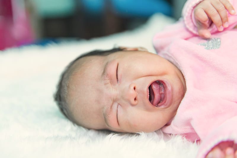 An infant girl is crying because her stomach is upsetting her