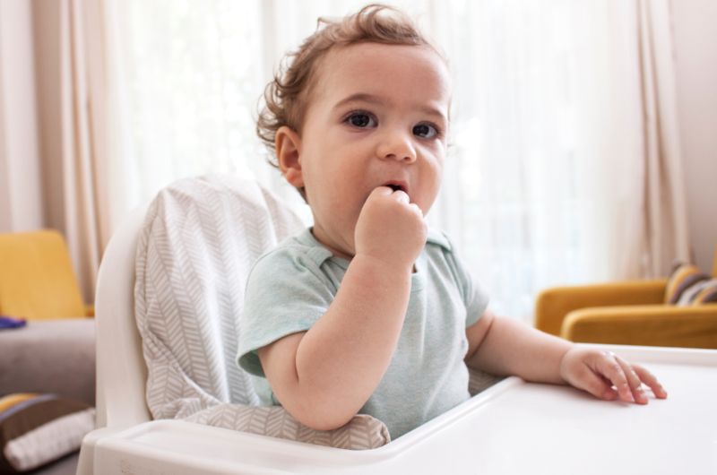 A one-year-old toddler is using his hand to bite on and relieve his teething pain