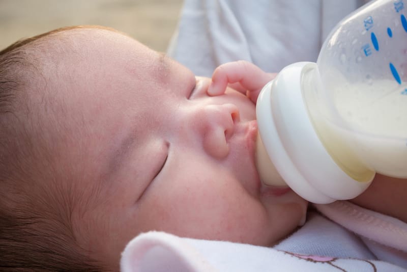 A sleepy baby is drinking formula milk from a bottle