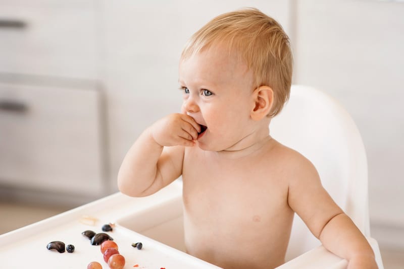 A one year old is eating cold grapes to relieve his teething pain