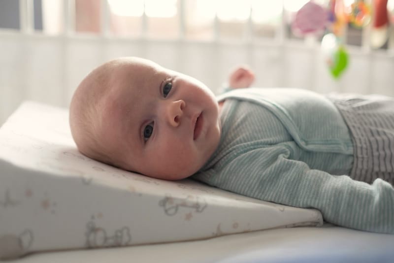 An infant baby is laying on an elevated pillow to help with his frequent spit-ups
