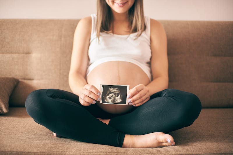 A pregnant woman is happily holding her ultrasound picture of her baby