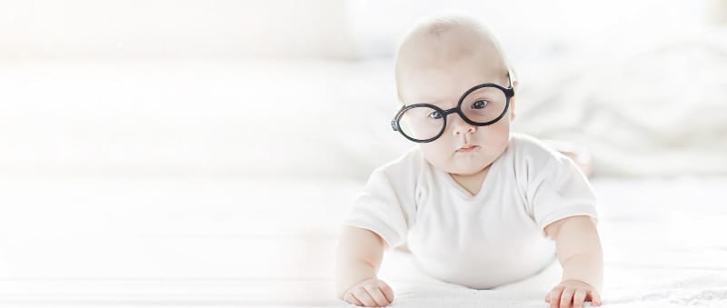 An infant baby boy is wearing black glasses while doing tummy time