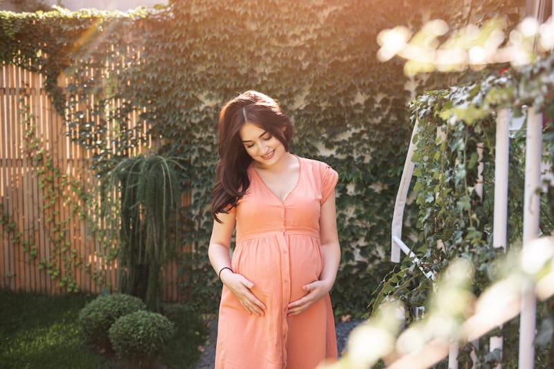 A pregnant woman is outside on a warm and beautiful day and is touching her womb to bond with her baby