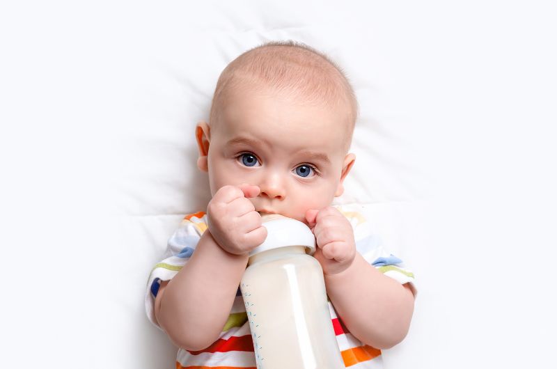An infant boy is drinking milk from his bottle