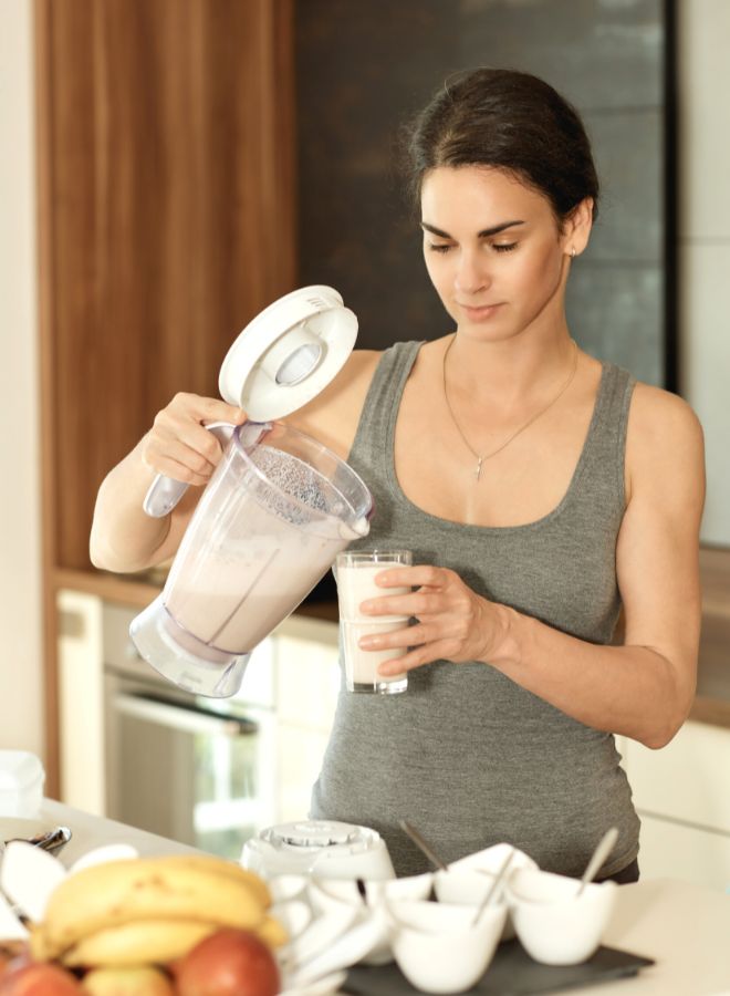 A newly pregnant woman is pouring a glass of protein shake that she just blended