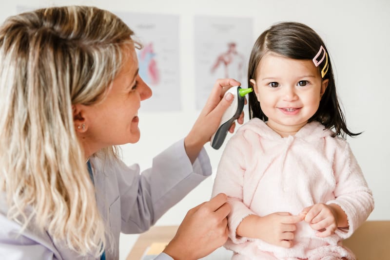 A pediatrician is checking a toddler girls ear for possible ear infection or earwax buildup