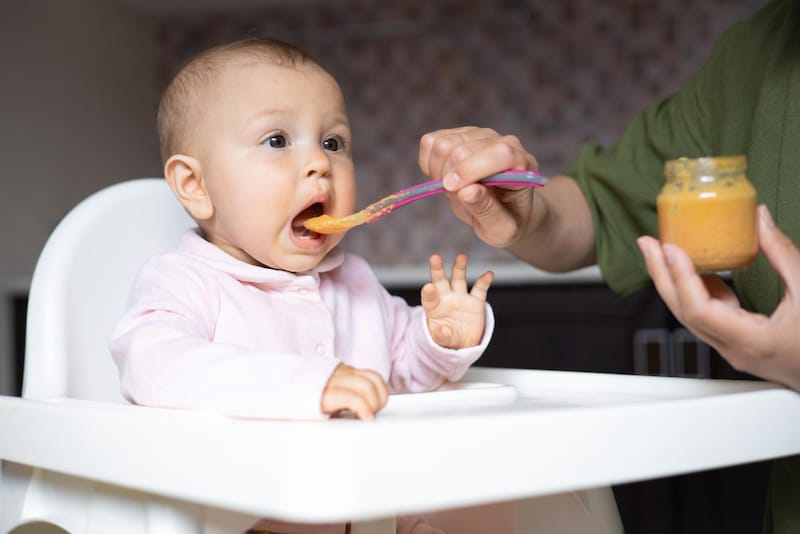Mom is feeding her infant daughter some high fiber vegetable puree to help prevent constipation