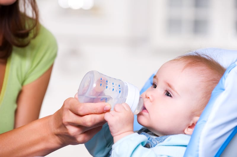 Mom is bottle-feeding her infant son some water to help keep him hydrated
