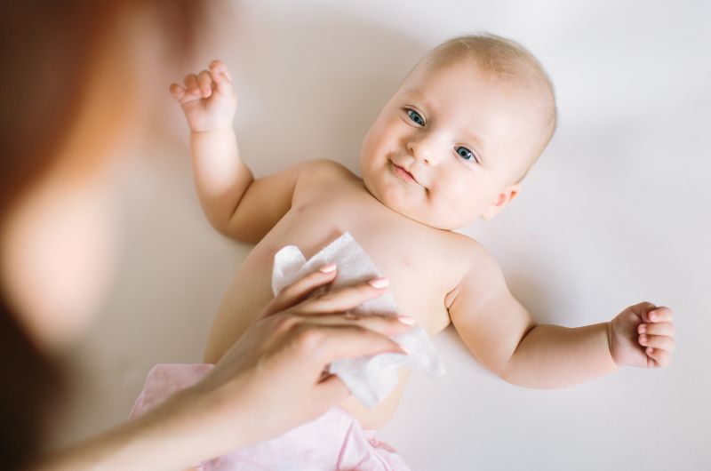 Mom is using a sensitive skin safe wet wipe to clean a small mess on her infant baby's belly.