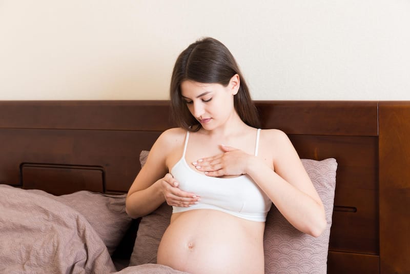 A pregnant woman is massaging her sore breasts, which are changing over the course of her pregnancy.