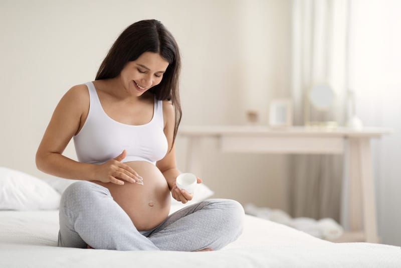 A pregnant woman is applying pregnancy-safe lotion on her pregnant belly