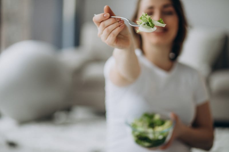 A pregnant woman is eating a small bowl of salad to help change her diet and ease her pregnancy heartburn