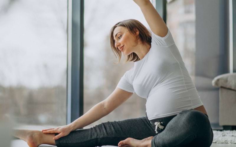 A young pregnant woman is practicing yoga as an alternative to using a back massager to ease her back pain and find relaxation.