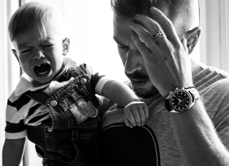 A frustrated dad is trying to console his upset and crying toddler son