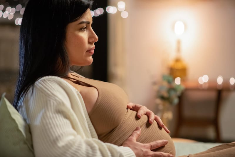 A pregnant woman in her third trimester is sitting down feeling uncomfortable because of her big baby bump