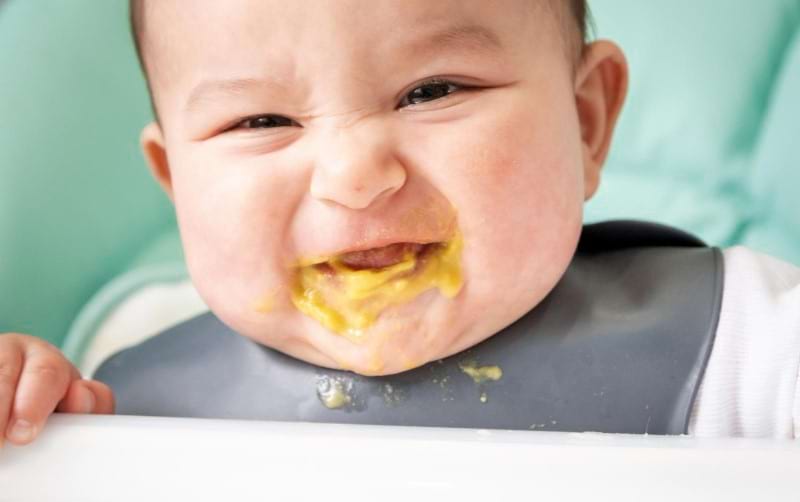 A happy baby is spitting up baby food