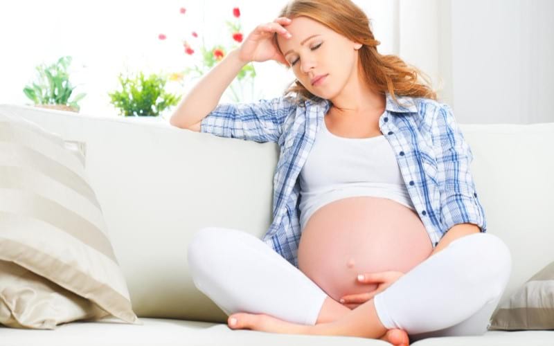 A pregnant woman has headaches due to foodborne illness by eating something undercooked or bad.