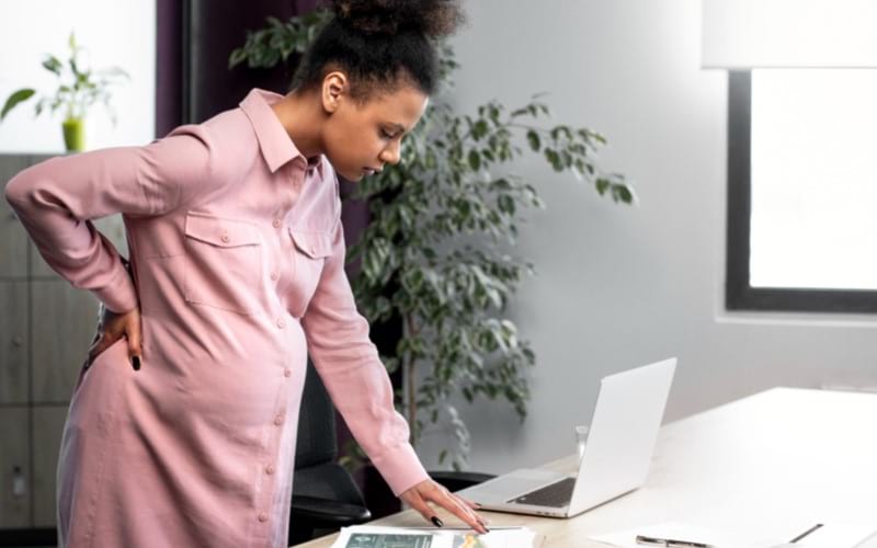 A young pregnant woman is feeling lower back pain while working in the office. 