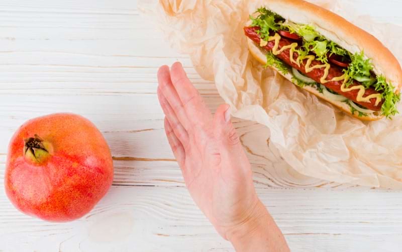 A woman's hand is trying to remove a hot dog showing how processed food is bad for a pregnant mother. 