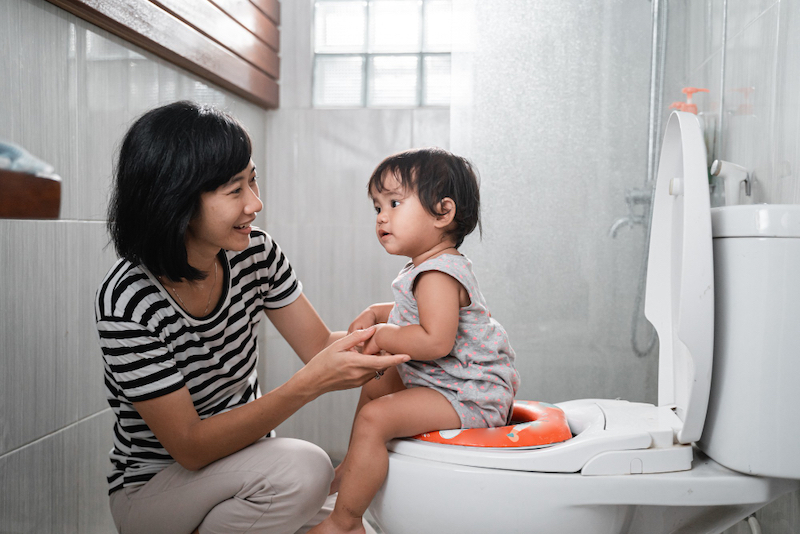 Mom is practicing potty training with her toddler daughter by spending time sitting on the toilet to get comfortable with it.