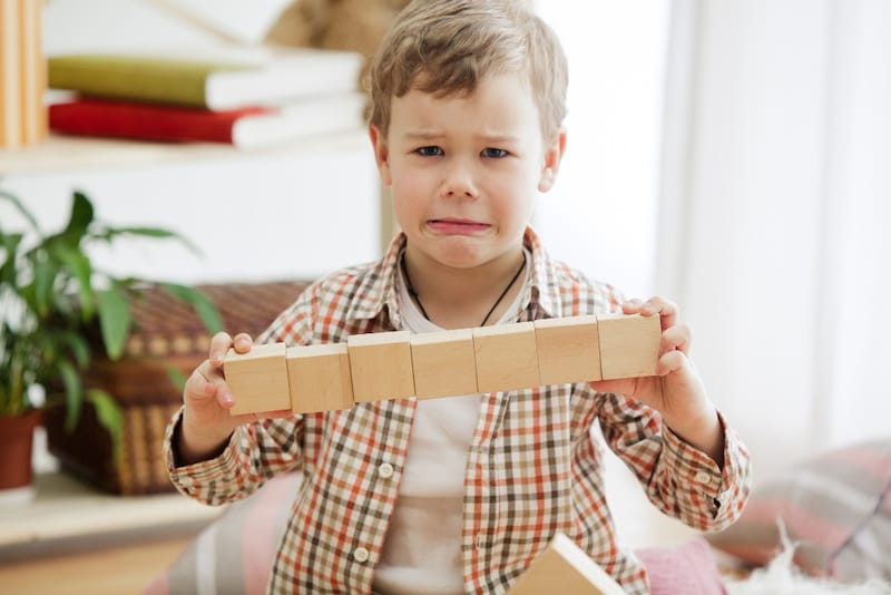 A toddler boy looks frustrated as he's trying to do the same thing with his blocks over and over again.
