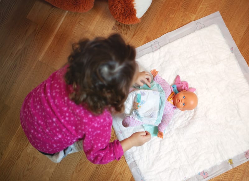 A toddler girl is getting comfortable with potty training by practicing the concept with her toy doll