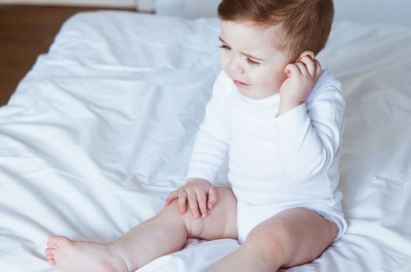 A toddler boy is itching his ear due to ear pain.