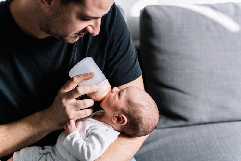 A dad is bottle feeding formula milk to his baby boy