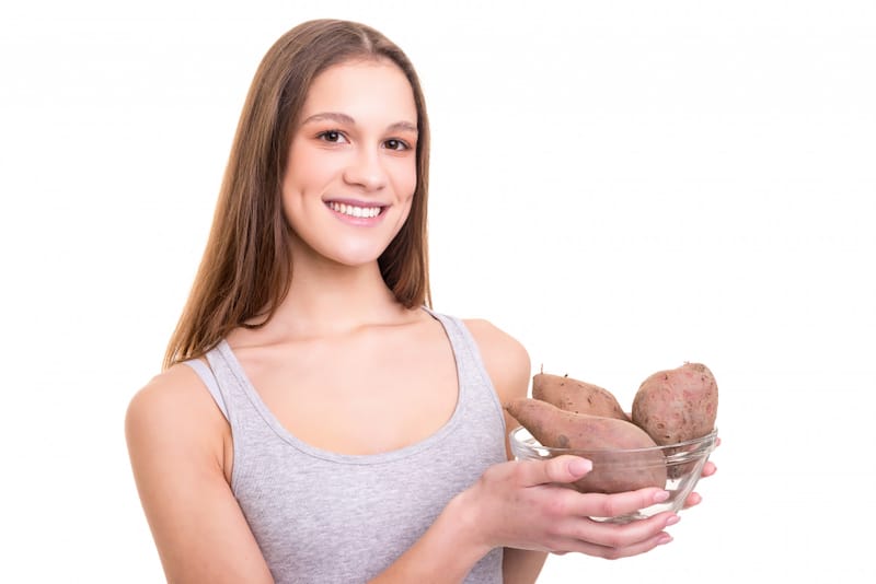A young mom is smiling and holding a bowl of sweet potatoes