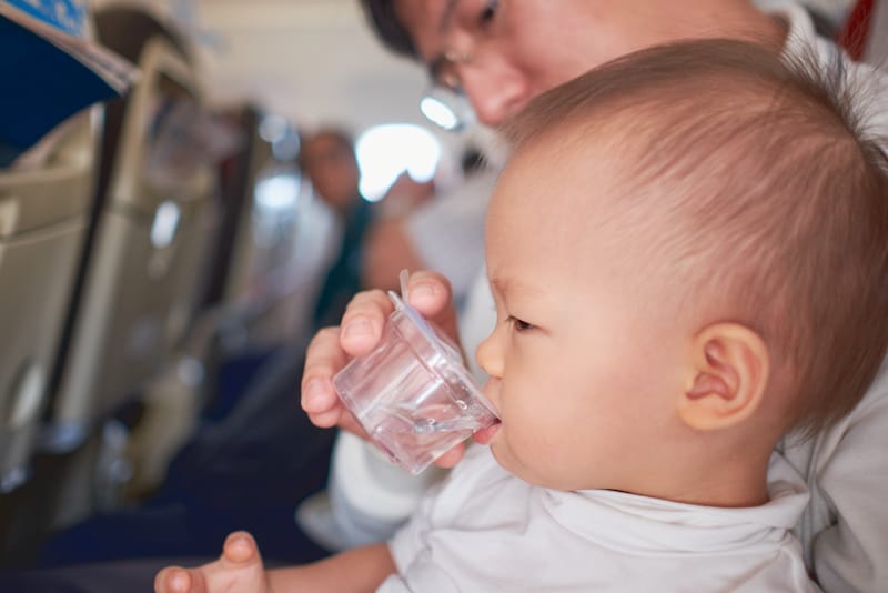 Dad is helping his infant son drink water from a cup
