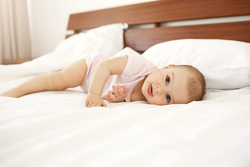 An infant girl is on a bed practicing rolling over from her back to her tummy