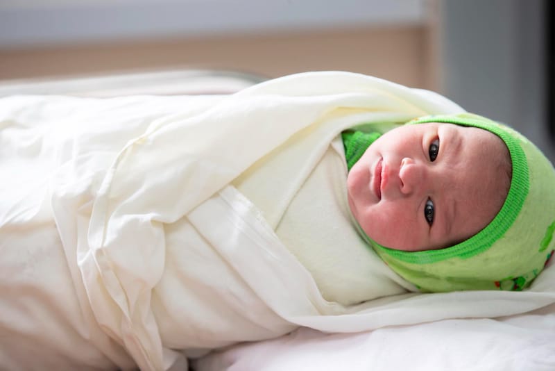 A swaddled newborn is laying on his back looking around