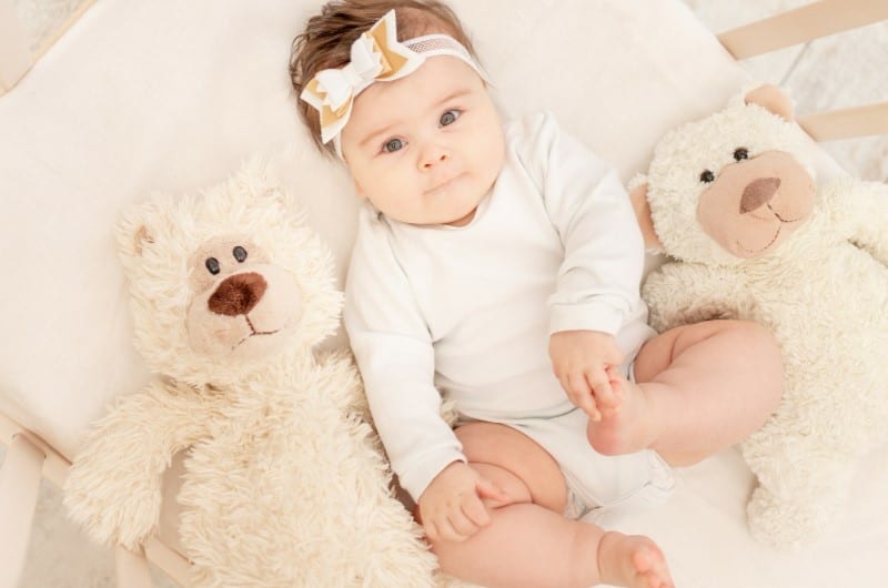 Toddler in the crib is surrounded by stuffed toys, which can cause suffocation while sleeping. 
