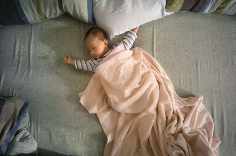 Cute newborn baby sleeping in a huge bed covered with blanket. 