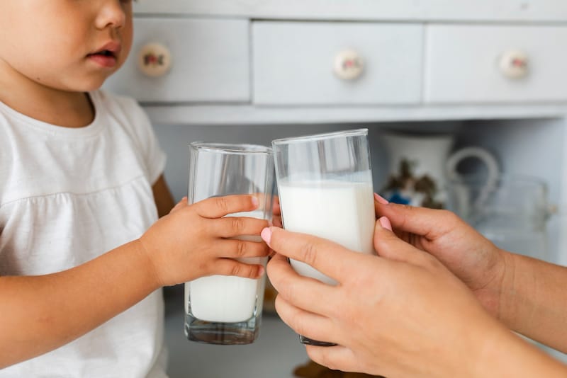 A mom and her toddler daughter are doing a "cheers" with their glasses of milk